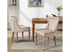 Conjunto de 2 sillas de terciopelo beige con patas de madera curvadas y remaches dorados.